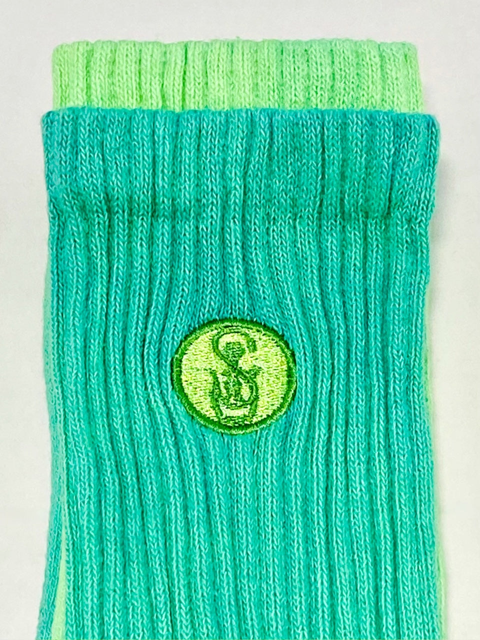 Green hand dyed crew sock embroidered with the Soles Unseen LLC logo.