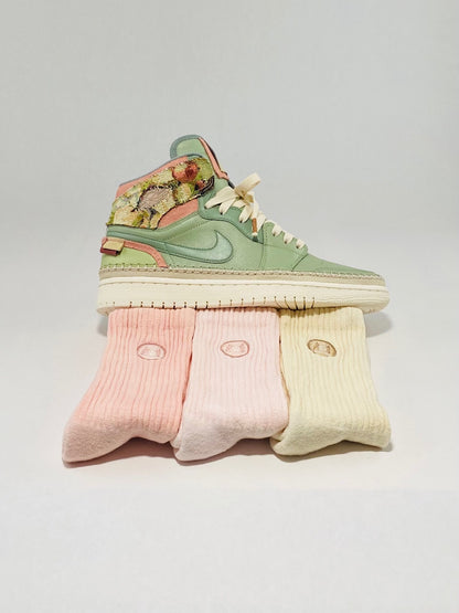 Custom painted green shoes sitting on three pairs of pink and tan crew socks.