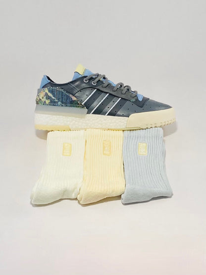 Custom painted grey shoes sitting on three pairs of yellow and blue crew socks.